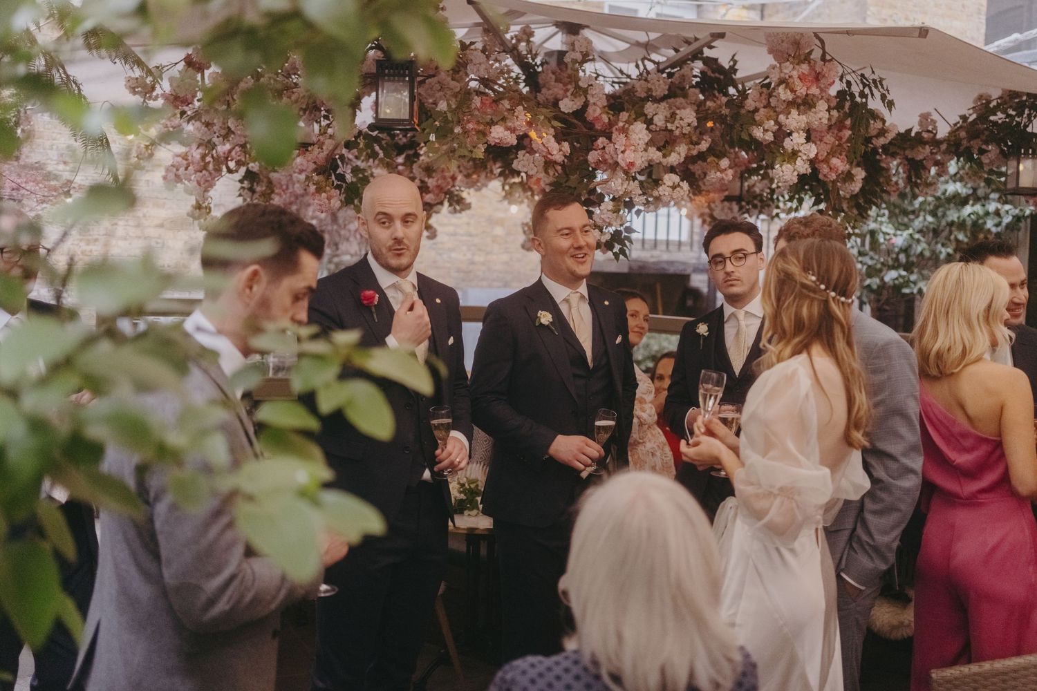 Wedding guests mingling and socializing under romantic floral arrangements at an evening reception.