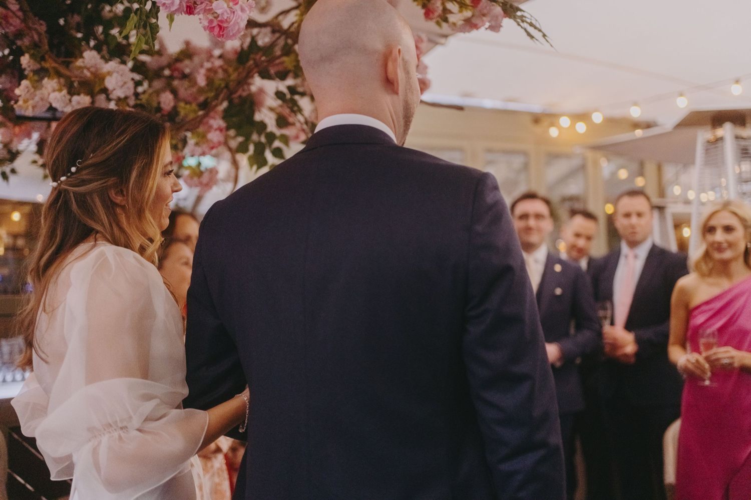 Back view of wedding guests gathered for a toast under cherry blossom decorations.