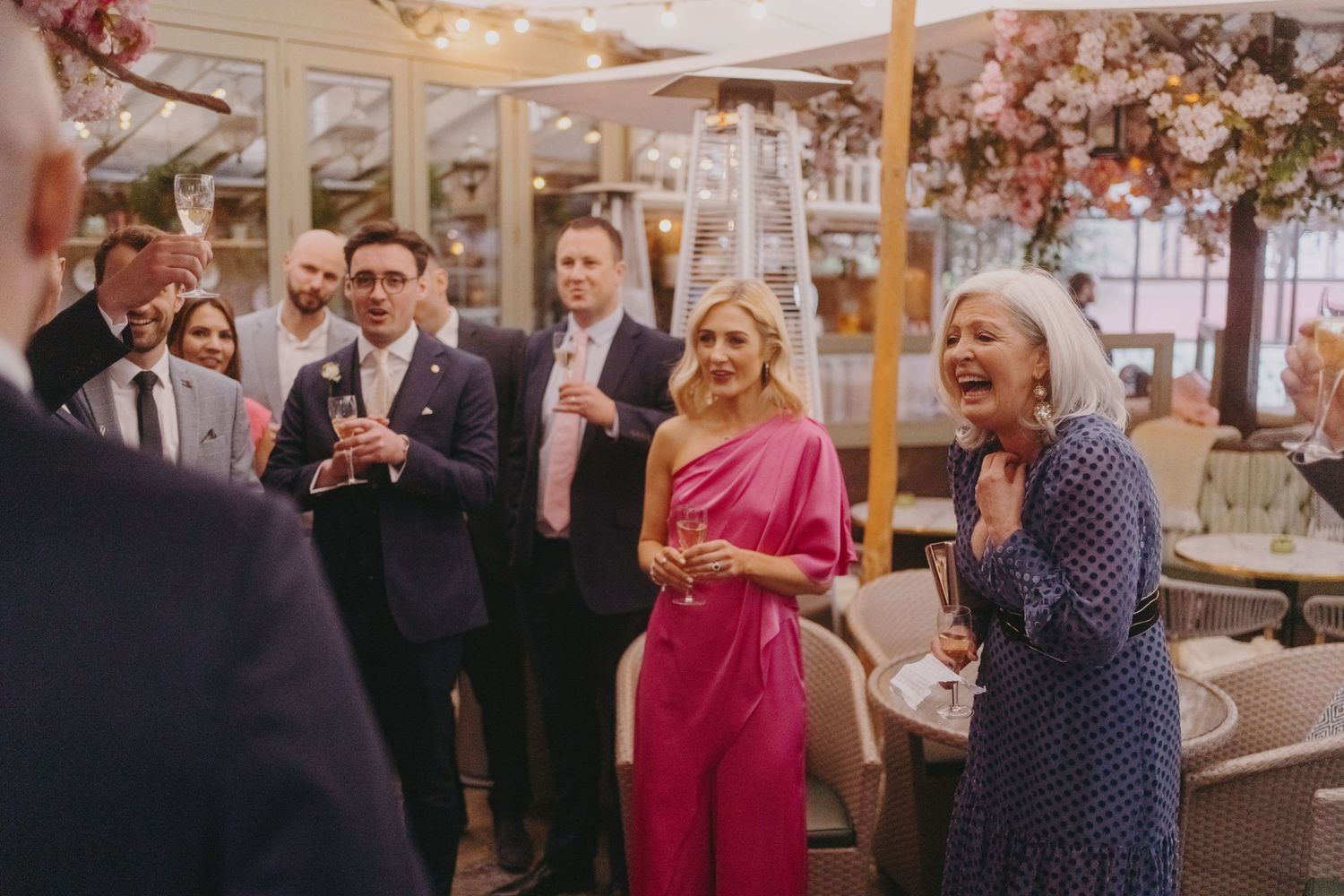 Wedding guests enjoying drinks and conversation under floral decorations at an outdoor reception.