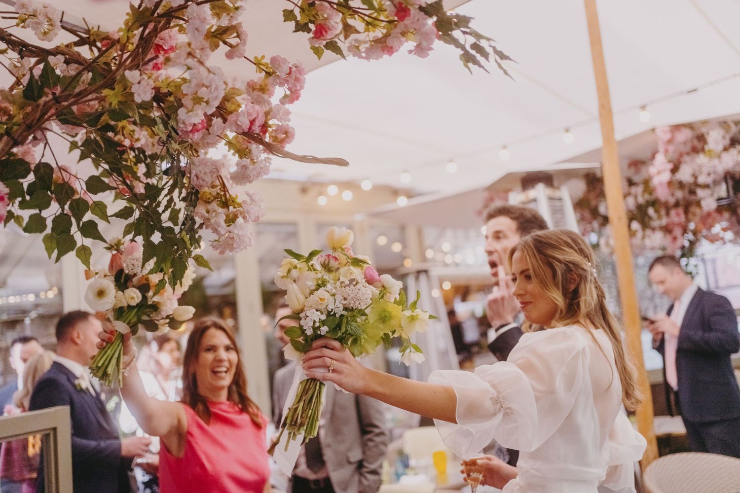 Wedding celebration under a floral-adorned tent with pink blossoms and festive decor.