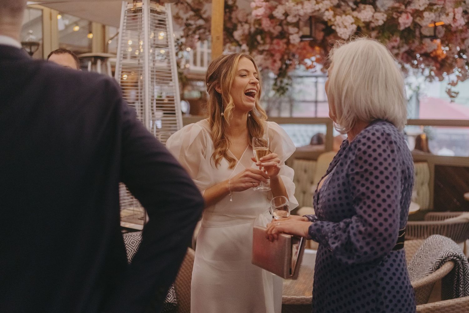 Guests enjoying laughter and conversation at an outdoor wedding reception under floral decor.
