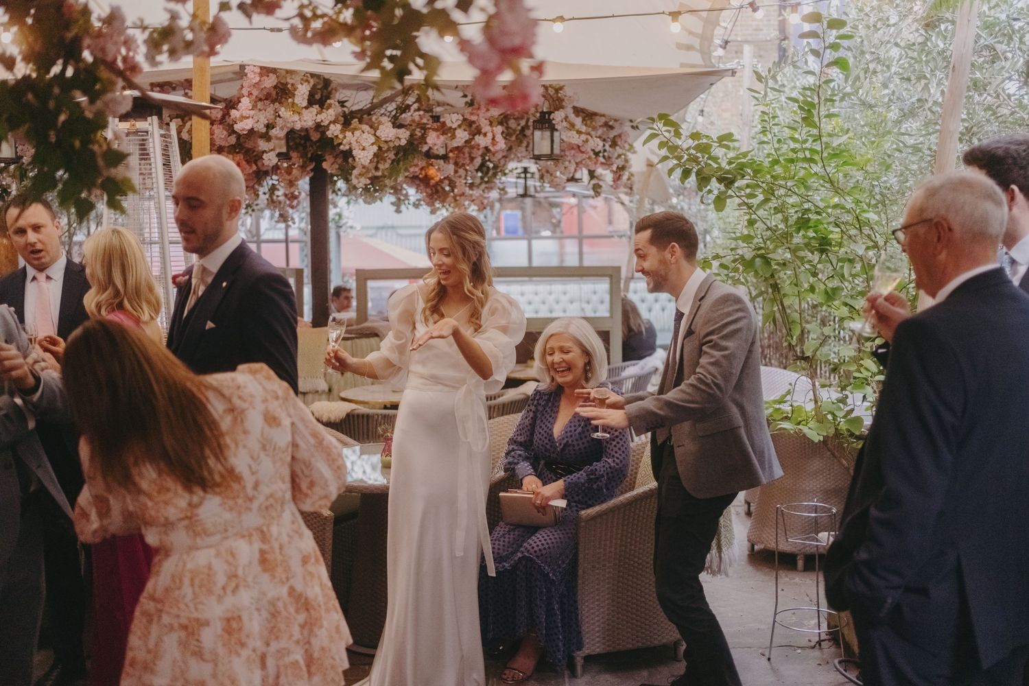 Wedding celebration at an indoor-outdoor venue with guests mingling under pink floral decor.