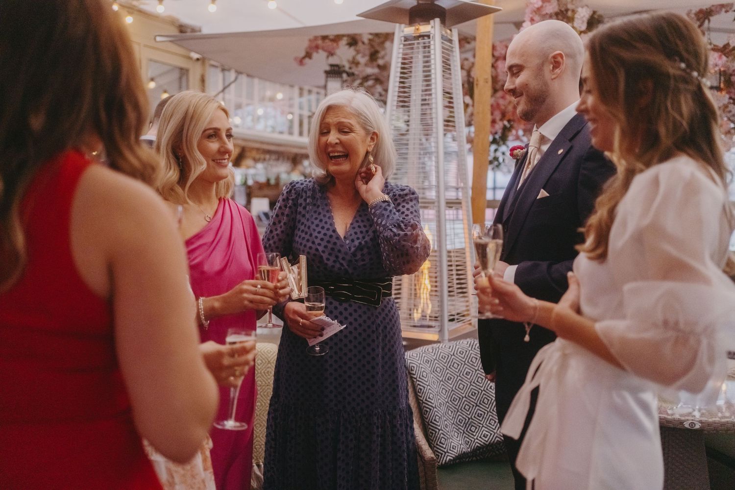 Wedding guests share laughter and drinks during an indoor reception.