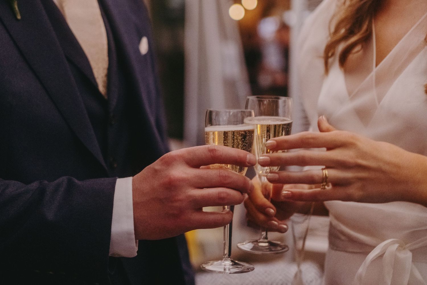 Hands clink champagne glasses in an elegant wedding toast moment.