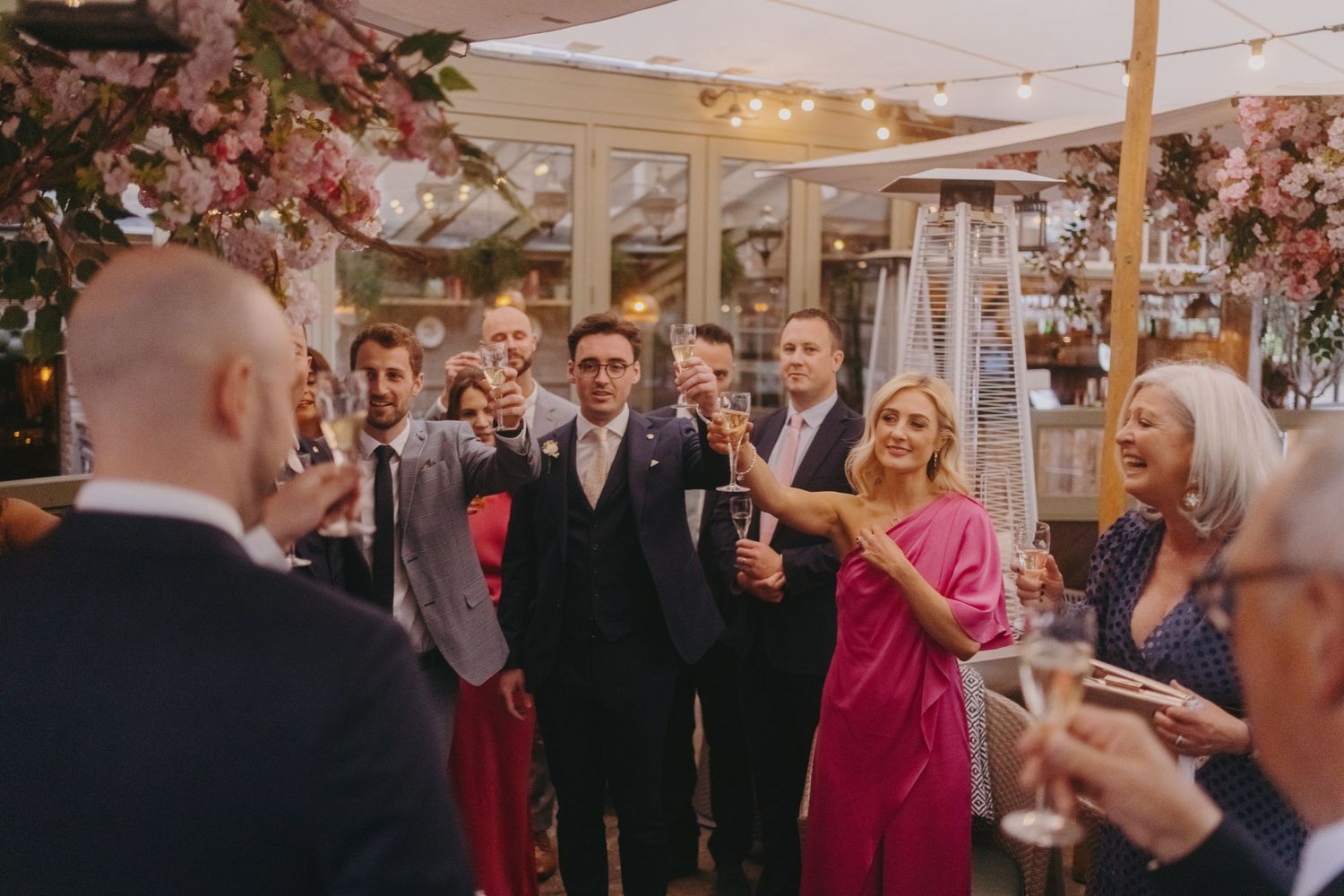 Wedding celebration with guests toasting under floral decorations and string lights.