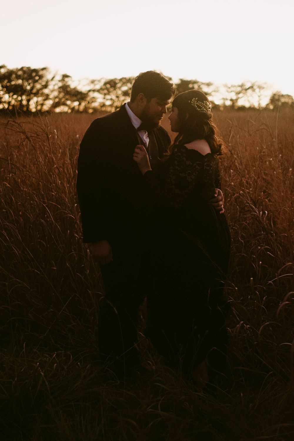Intimate silhouette of couple in dark clothing against sunset in tall grass field.
