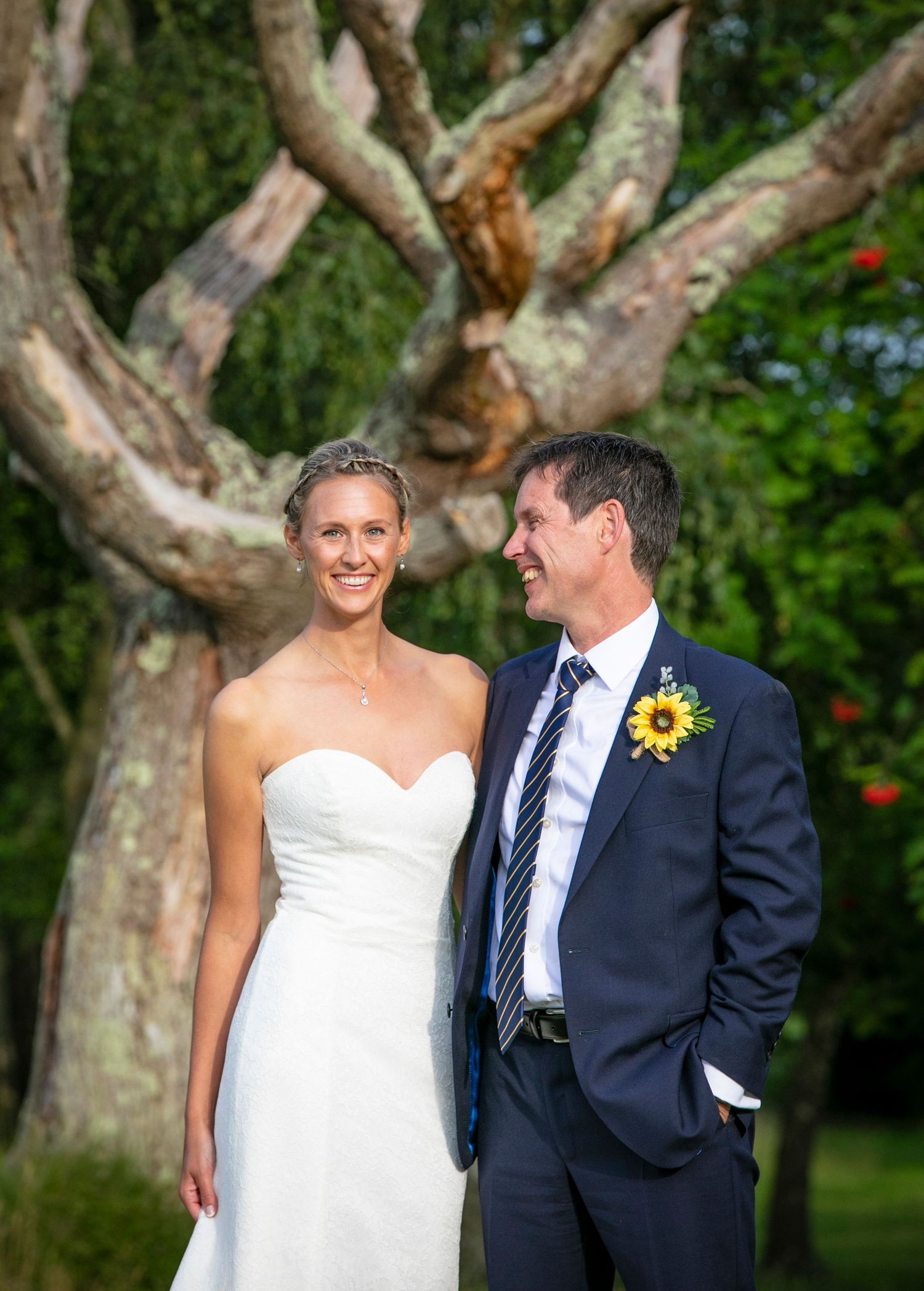 Wedding couple sharing a candid moment under large branching trees.