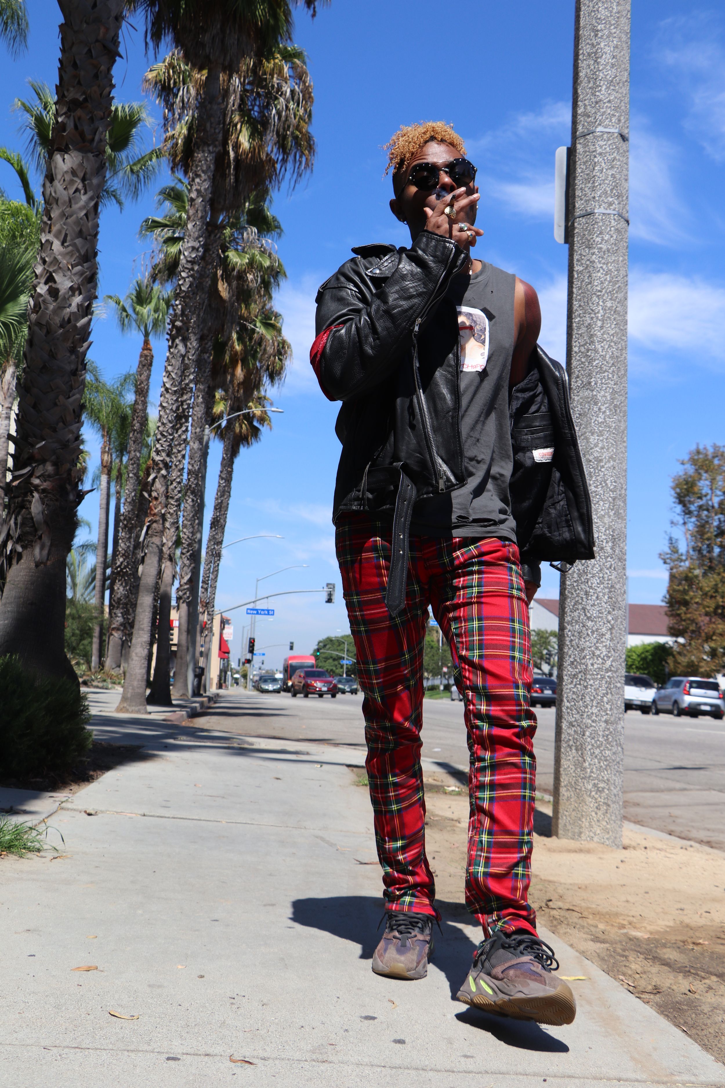 Street style portrait with plaid pants and leather jacket against palm tree background.