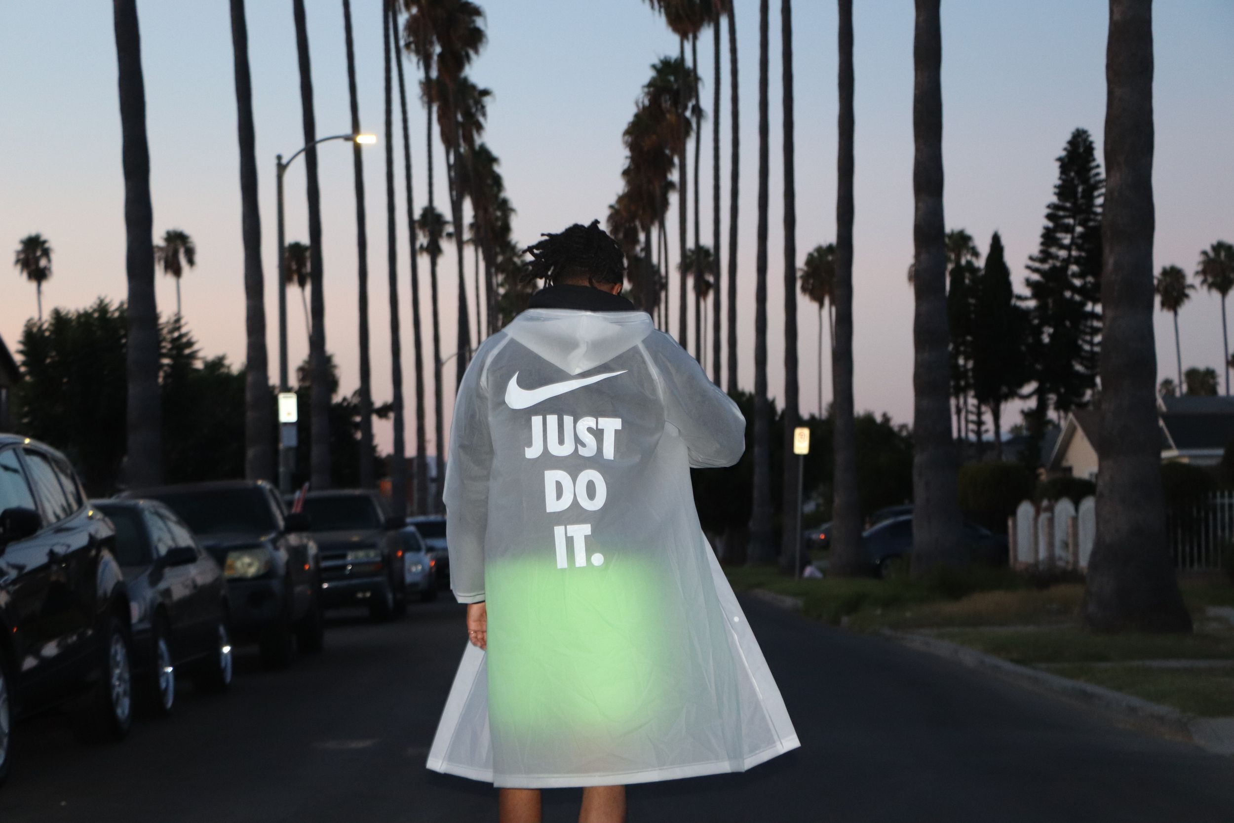 Glowing Nike 'Just Do It' shirt illuminated at dusk on palm tree-lined street.