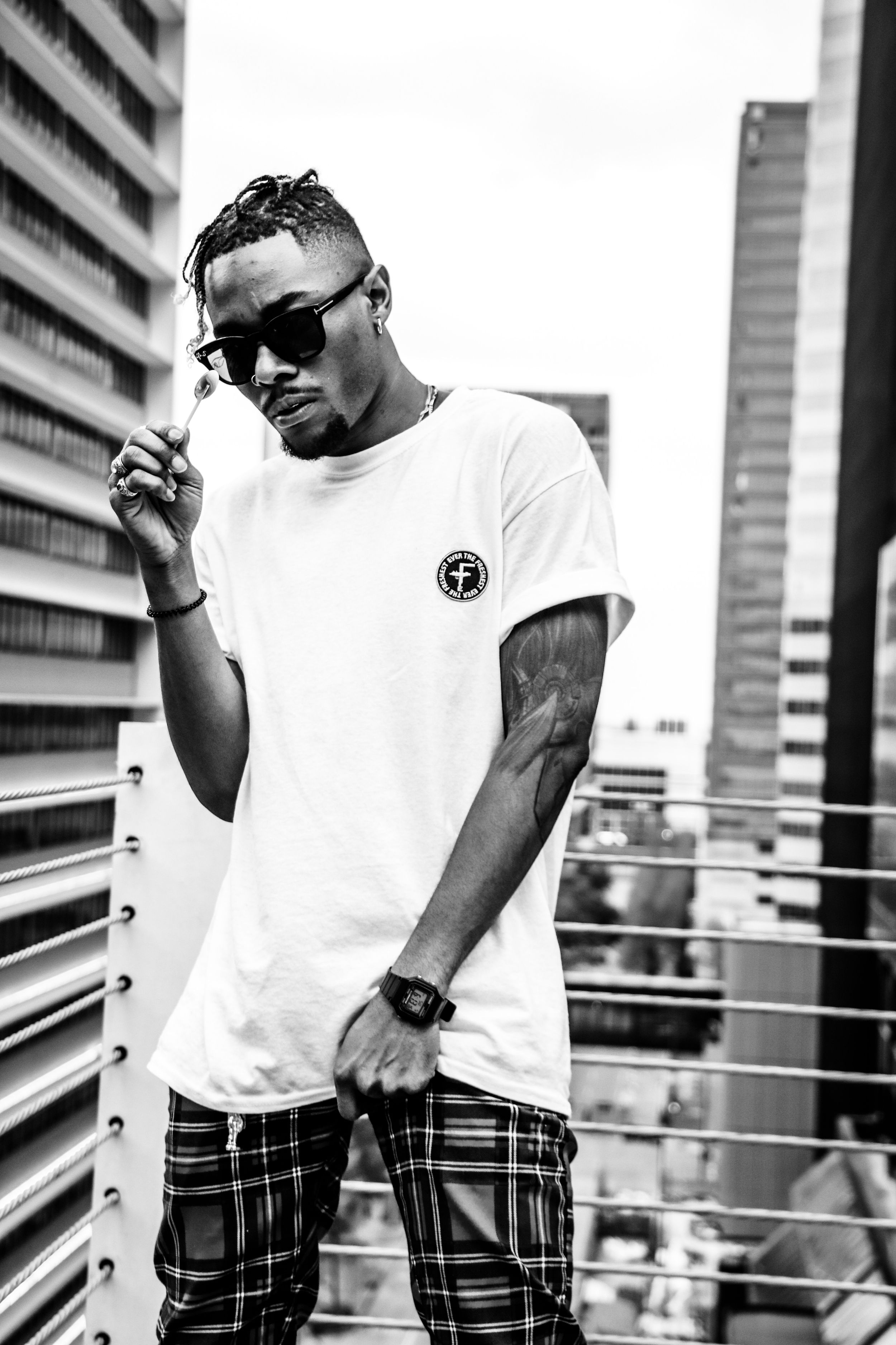 Athletic figure in sunglasses and white t-shirt poses against urban backdrop of tall buildings.