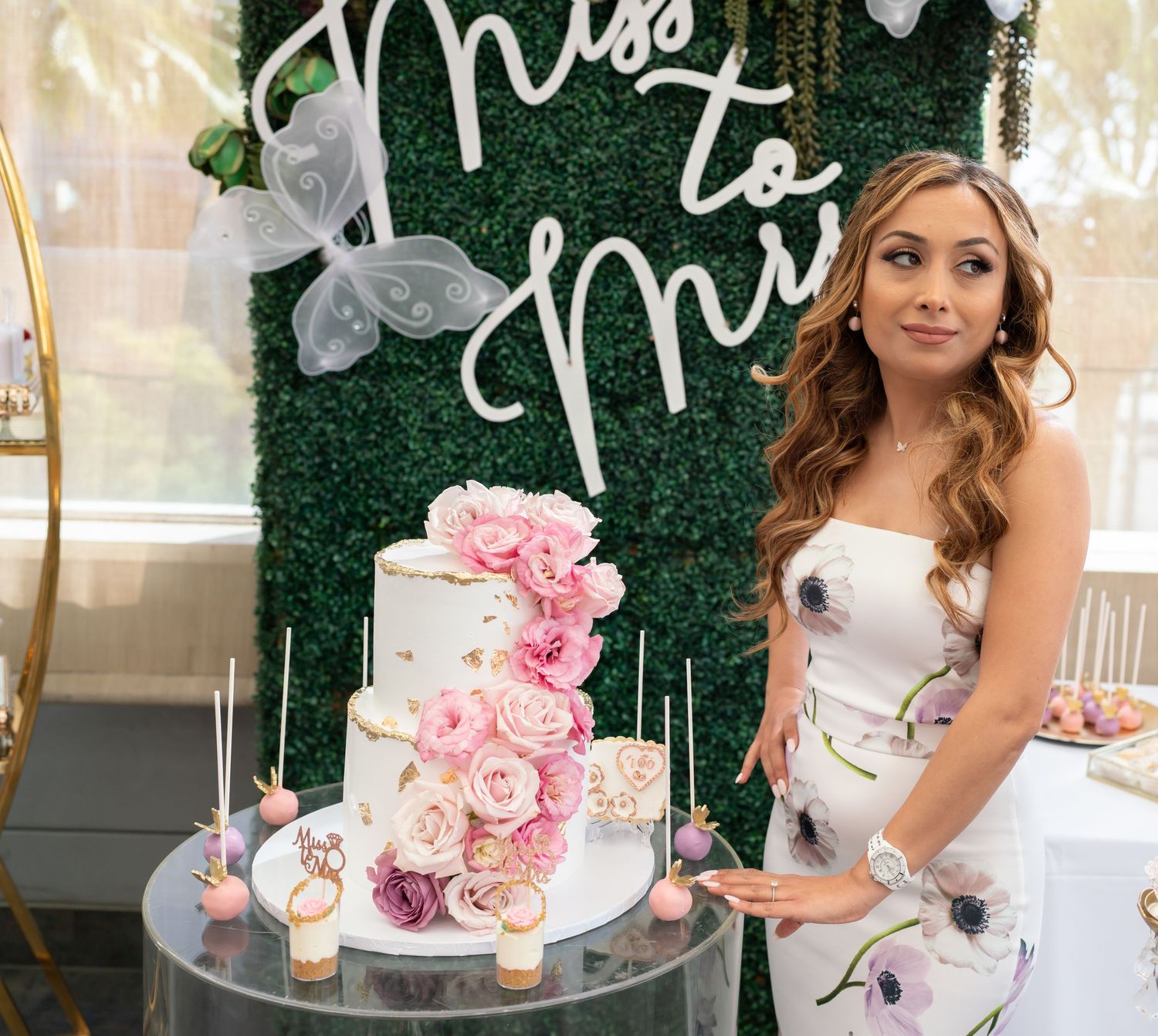 Elegant bridal shower setup with floral cake and 'Miss to Mrs' greenery wall backdrop.