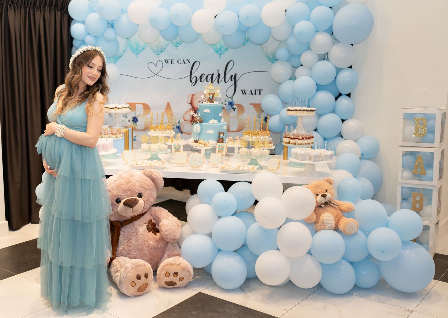 Baby shower dessert table decorated with blue balloons, plush bears, and sweet treats.