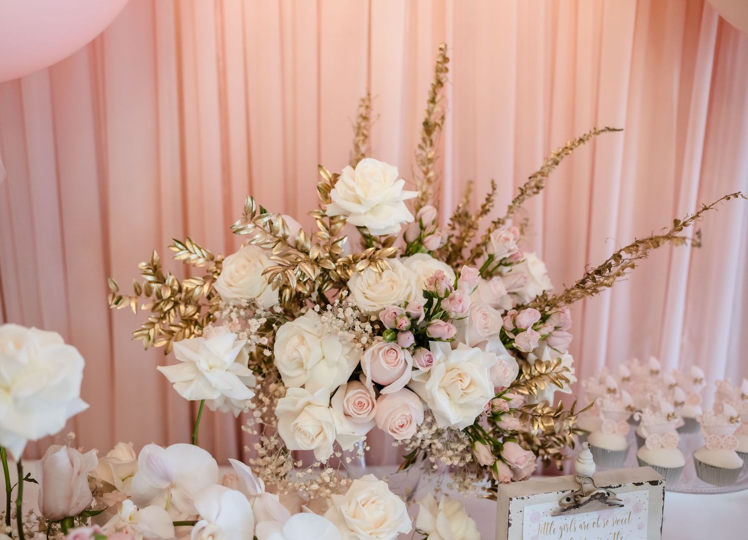 Romantic floral arrangement with white roses and delicate branches against pink drapery.