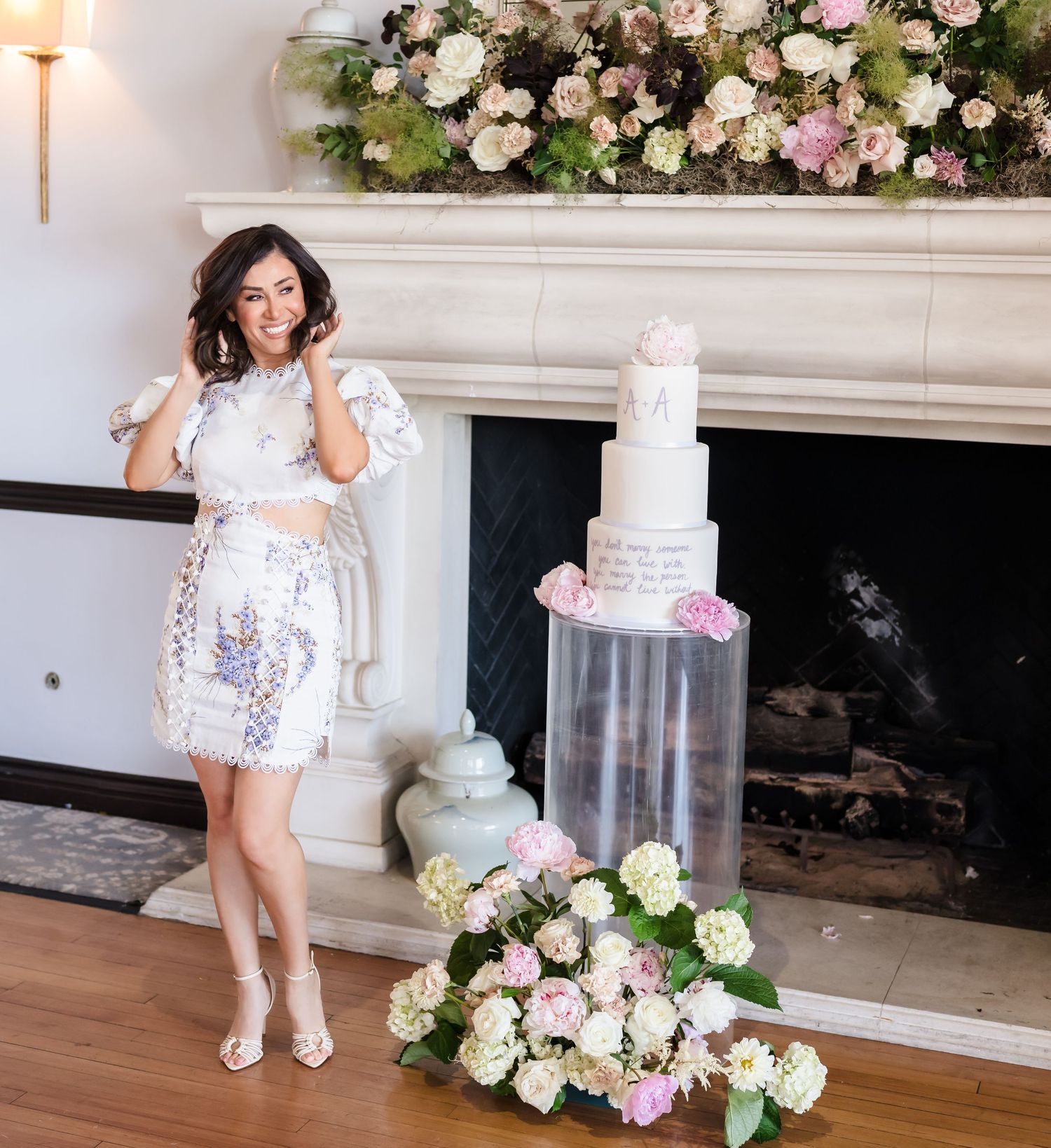 A maternity photoshoot features a white floral dress and elegant cake display by a decorated fireplace.