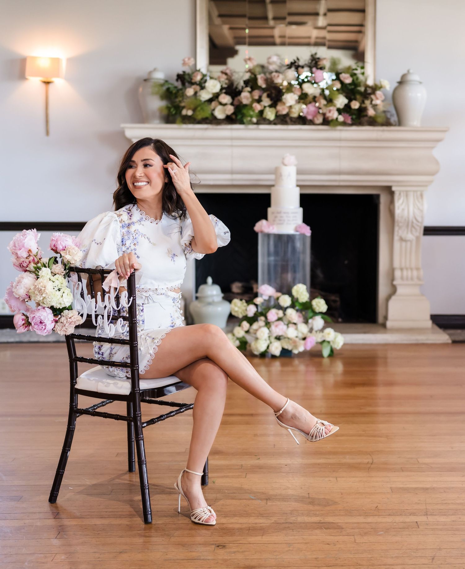 An elegant maternity scene with a woman seated by a fireplace surrounded by floral arrangements.