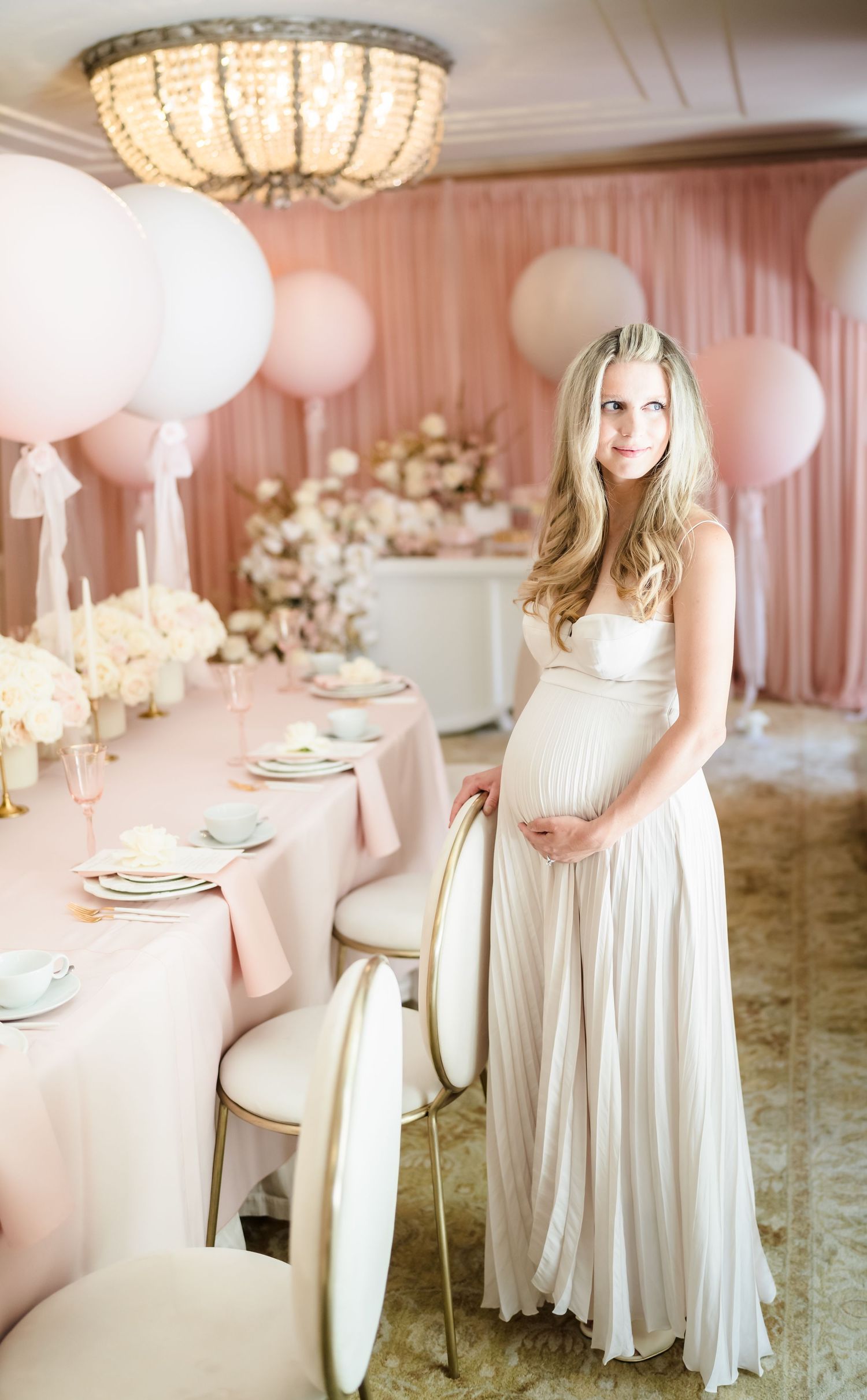 Elegant baby shower setup with pink table settings and crystal chandelier overhead.