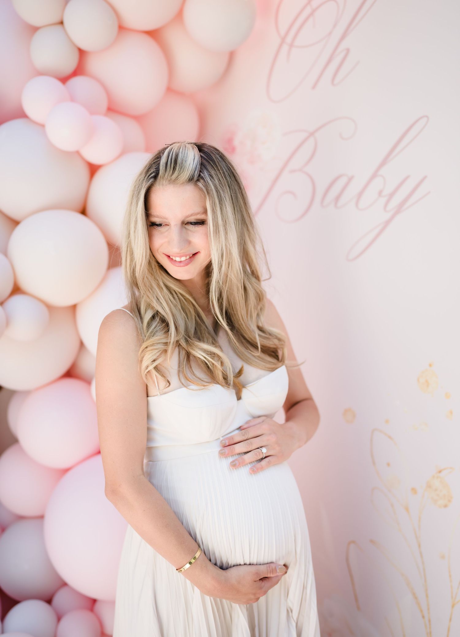 Baby shower photo with pink balloon arch and elegant maternity styling.