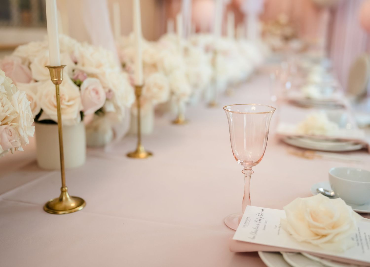 Elegant table setting with pink glassware, gold candlesticks and white floral centerpieces.