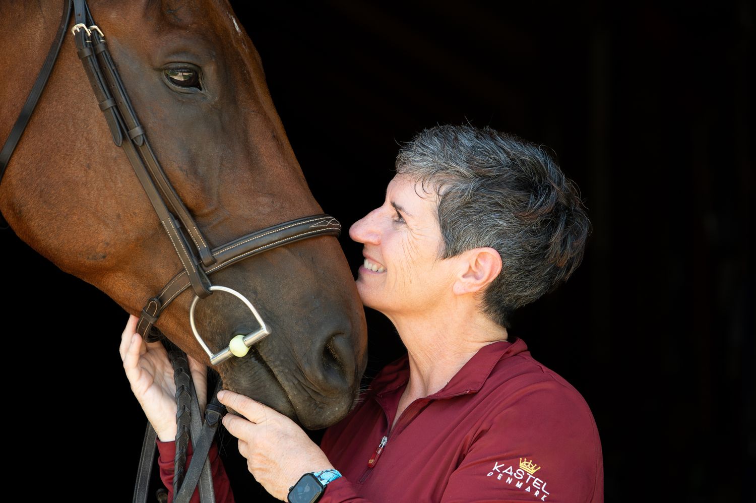 A tender moment between a brown horse and someone in burgundy attire.