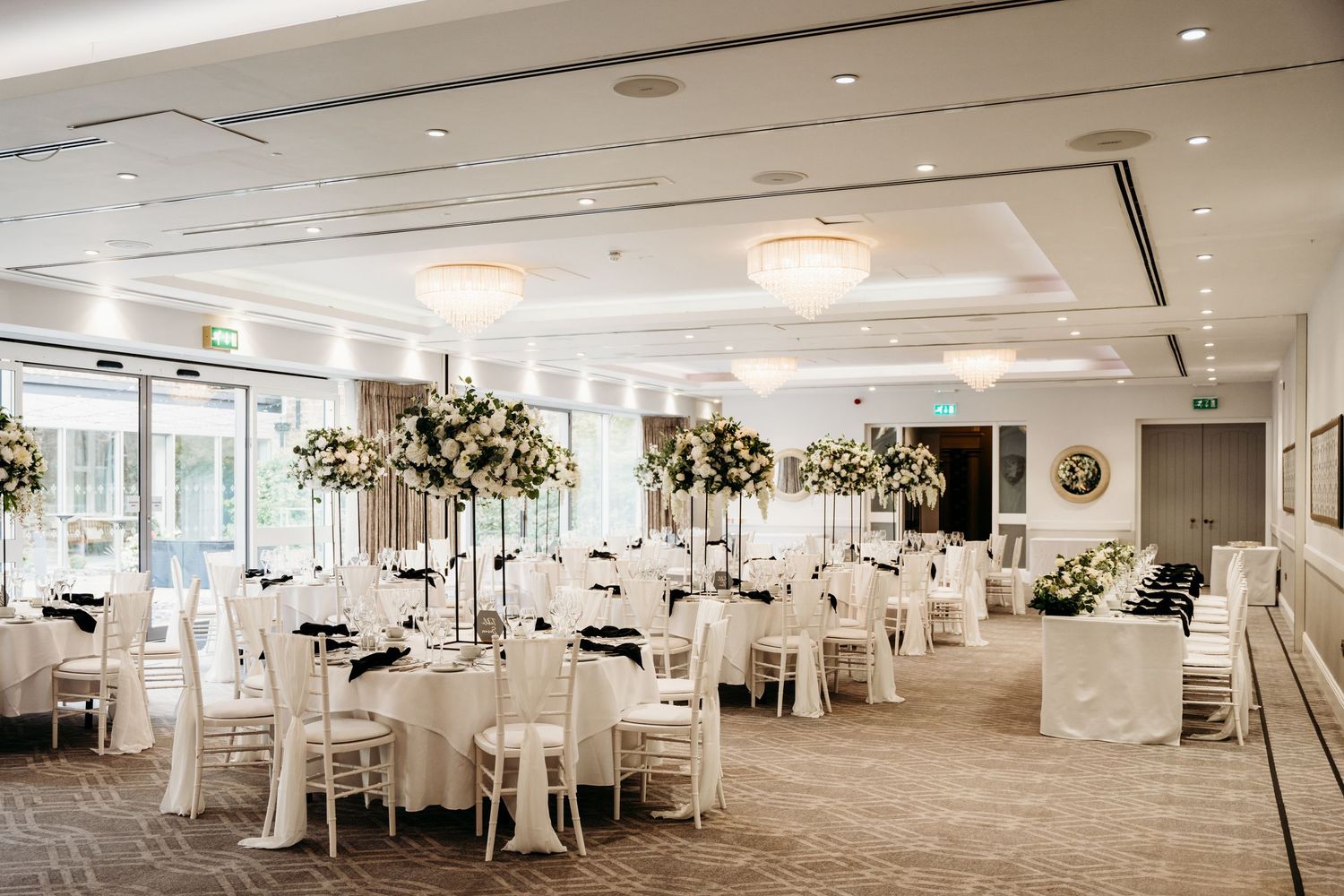 Elegant white wedding reception room with tall floral centerpieces and round tables.