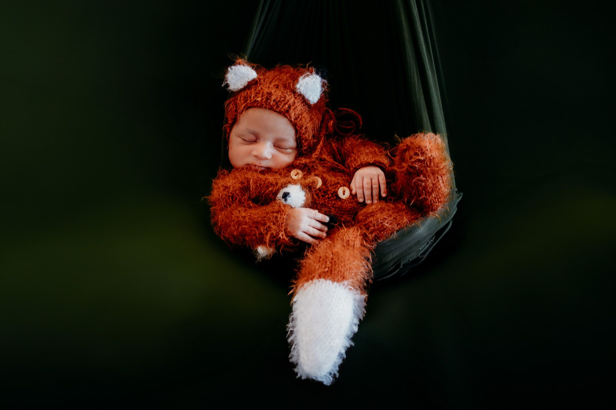 Sleeping newborn wearing a plush fox costume in a hanging prop.
