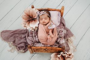 Vintage-styled newborn photography setup with wooden props and mauve floral accessories.