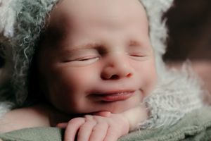Smiling sleeping baby wrapped in soft mint green fabric.