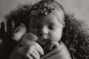 Peaceful sleeping newborn in gray wrap with delicate headband.