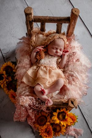 Newborn sleeping on rustic wooden bed with pink tulle and sunflowers.