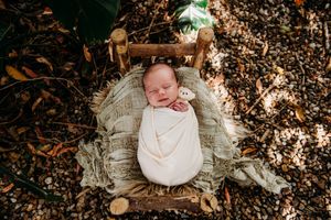 Outdoor newborn photography with baby lying on white blanket surrounded by autumn leaves.