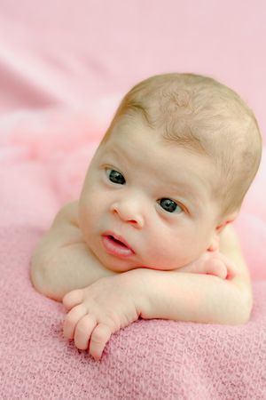 Baby with bright blue eyes lying on pink textured blanket in close-up portrait.