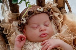 Peaceful sleeping baby wrapped in soft beige fabrics with floral accents.