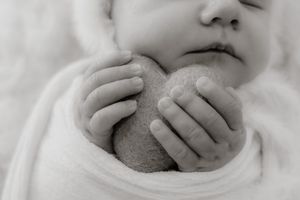 Close-up black and white image of tiny hands holding a round object against white fabric.