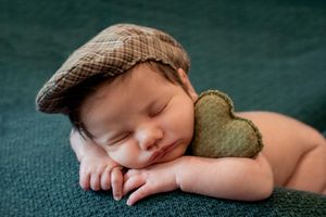 Gentle sleeping pose on dark green textured fabric with newsboy cap.