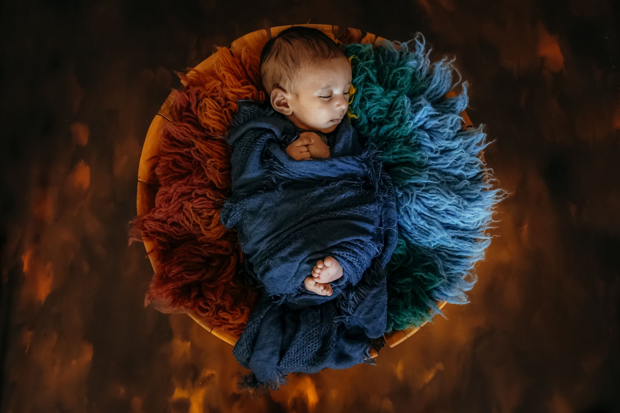 Artistic newborn portrait with dramatic lighting featuring blue and orange tones.