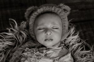 Black and white portrait of sleeping newborn nestled in soft textured bedding.