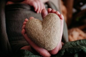 Hands gently holding a soft plush heart against dark fabric.