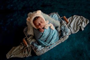 Newborn baby wrapped in blue swaddle on dark textured background.