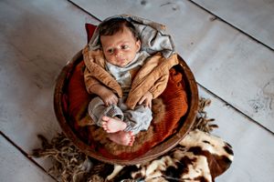 Sleeping baby posed in rustic wooden bowl with soft decorative elements.