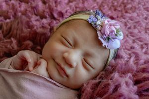 Sleeping baby on pink textured blanket wearing floral headband.