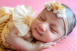 Peaceful sleeping baby with cream colored bow headband on pink background.