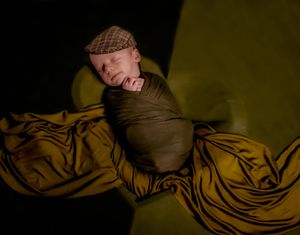 Sleeping newborn wrapped in dark fabric against yellow textured background.
