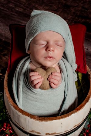 Newborn wrapped in gray fabric holding teddy bear in wooden basket.