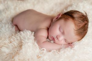 Sleeping newborn baby lying peacefully on white fluffy fur.