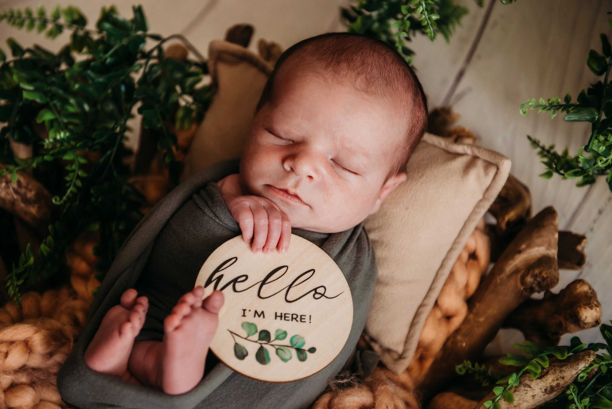 Rustic wooden setup with greenery and handwritten welcome sign for newborn photography.