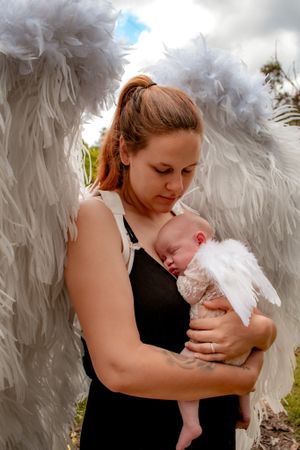 A tender moment captured between a mother and infant with ethereal white angel wings in the background.