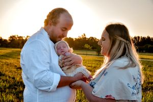 Family portrait silhouetted against a golden sunset in an outdoor field setting.