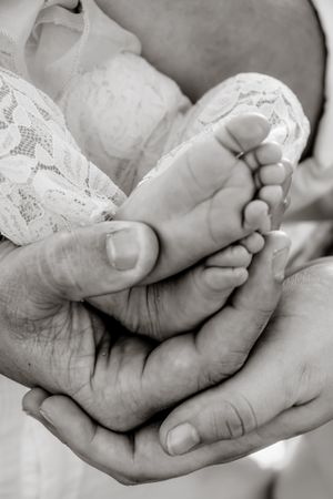 Black and white close-up of tiny baby feet being gently held in adult hands.