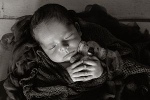 Black and white image of sleeping infant wrapped in knit blankets.