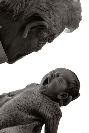 Black and white profile shot of elder looking down at yawning infant in sweater.